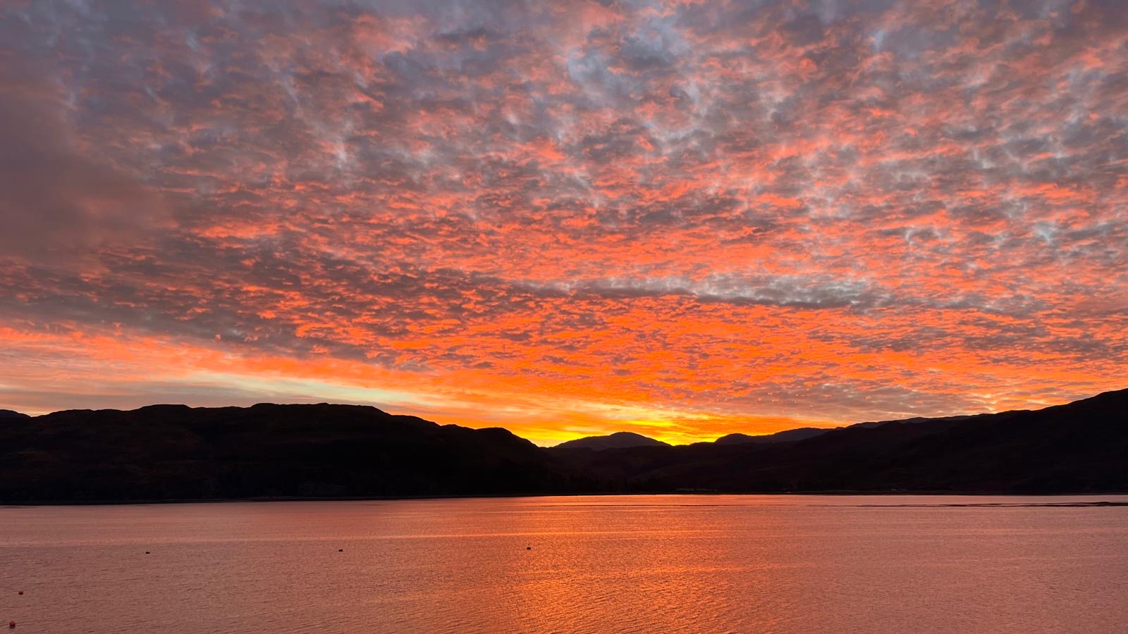 A vivid red sunset reflected across Loch Carron